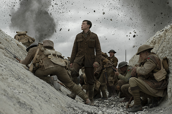 Soldiers in World War I uniforms crouch in a dirt trench as debris flies through the air from an explosion.