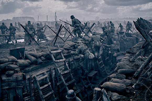 Soldiers in helmets move through a muddy, war-torn landscape filled with trenches and wooden fortifications.