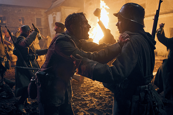Two soldiers in military uniforms grapple intensely amidst a chaotic, firelit nighttime battlefield.