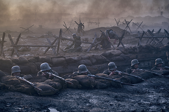 Soldiers in helmets aim rifles from a muddy trench behind sandbags under a smoky sky.