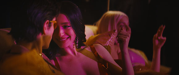 A man and a woman smile at each other in a dark room, while a third person sits in the background.