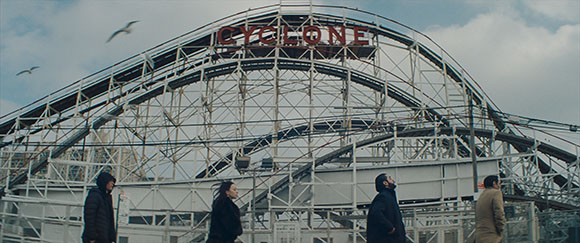 A large wooden roller coaster structure with a red sign reading CYCLONE under a cloudy sky.