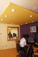 A person sits at a desk with monitors in a purple and yellow studio control room.