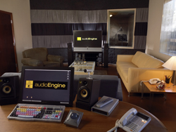 A computer monitor, speakers, and mixing console on a desk in a room with a sofa and armchair.
