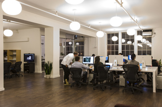 People sitting at desks with computers in a bright, modern office with large spherical pendant lights.
