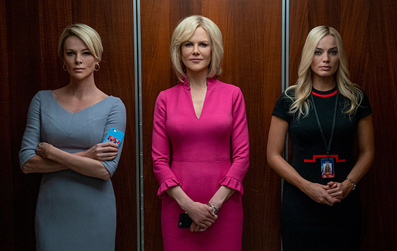 Three women in formal dresses stand against a dark wood paneled wall.