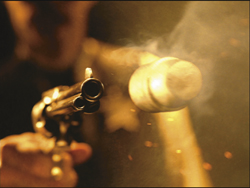 A close-up of a revolver being fired, showing smoke and sparks in a dark setting.