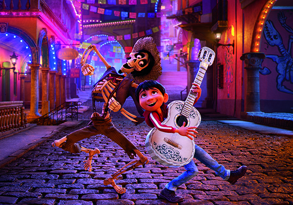 A boy with a guitar and a skeleton character dance joyfully on a cobblestone street at night.