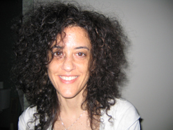 A smiling woman with voluminous, dark curly hair looking toward the camera.