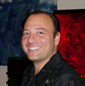 A smiling man with dark hair wearing a black button-down shirt.