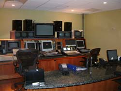A control room featuring several computer monitors, speakers, and audio mixing equipment on desks.