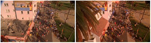 A crowded boardwalk with people walking past buildings and palm trees under warm sunlight.