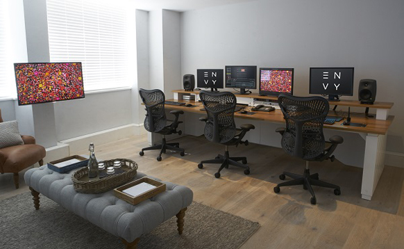 Three workstations with black ergonomic chairs and multiple monitors in a bright, modern office.