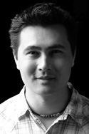 Black and white portrait of a man wearing a plaid shirt and a necklace.