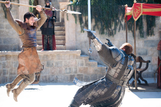 A man in brown tunic jumps with a spear while a knight in plate armor raises a sword.