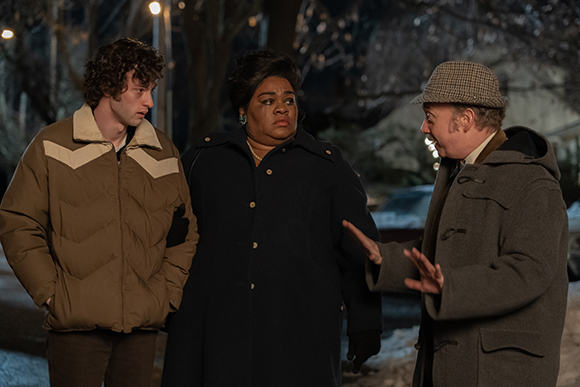A woman in a black coat and a man in a brown coat talk to a man in a tan jacket at night.