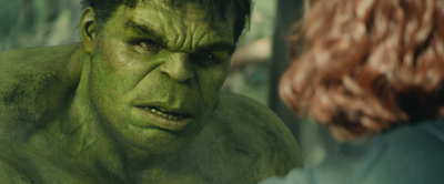 A large green muscular man with a furrowed brow stares intensely at a woman with wavy red hair.
