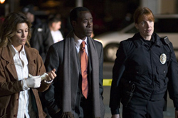 A woman in a brown coat, a man in a suit with a scarf, and a female police officer walking at night.