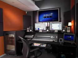 A professional editing suite with a large monitor displaying 'LA DIGITAL POST', mixing consoles, and studio monitors.