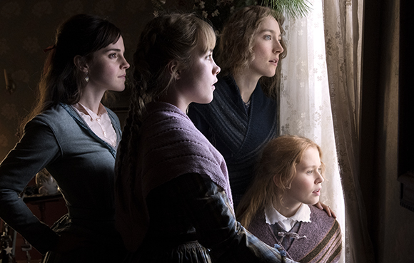 Four women in period clothing gaze intently out of a bright window in a dimly lit room.