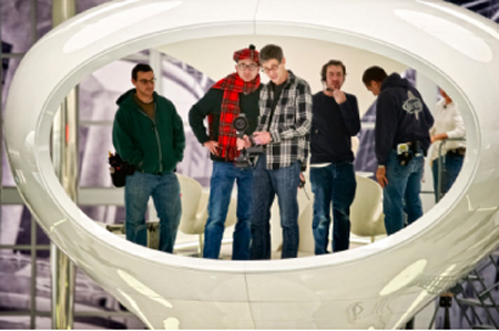 Five men stand together inside a large, white, ring-shaped architectural structure.