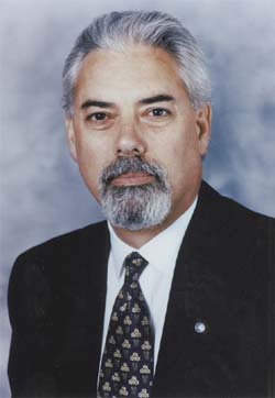 Headshot of a middle-aged man with gray hair, a gray goatee, wearing a dark suit and patterned tie.