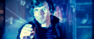 A man stares forward through a glass surface covered in glowing blue digital data and lines.