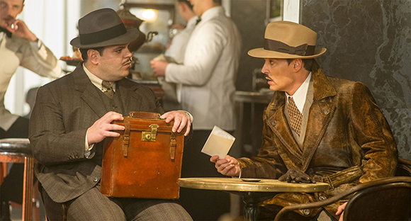 Two men in early 20th-century clothing sit at a cafe table with a leather briefcase and a small piece of paper.