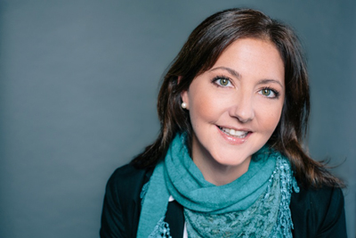 A smiling woman with brown hair wearing a teal scarf and a black jacket.