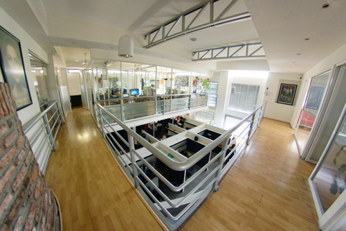 High-angle view of a two-story modern office with wooden floors, glass partitions, and white metal railings.