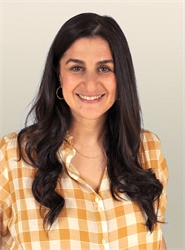 Smiling woman with long wavy dark hair wearing a yellow and white checkered button-down shirt.