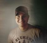 A smiling man wearing a dark baseball cap and a grey t-shirt with the word ELEMENT printed on it.