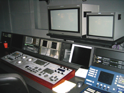 A control desk with multiple monitors, video editing consoles, and control panels in a dark studio.