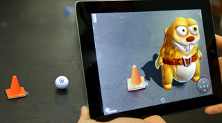 A person holds a tablet showing a cartoon character and a cone on a table via augmented reality.