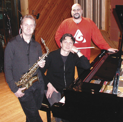 Three men pose in a studio with a saxophone and a grand piano.