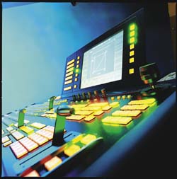 A close-up view of a professional broadcast control console with glowing yellow buttons and a large monitor.