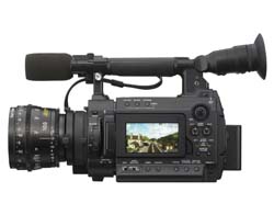 A black professional video camera with a large lens, top handle microphone, and an LCD screen showing a landscape.