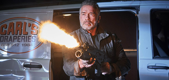 A man in a dark jacket fires a handgun, creating a large muzzle flash in front of a white van.