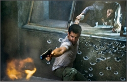 A man aims a handgun in a gritty setting while a person crawls in the background.
