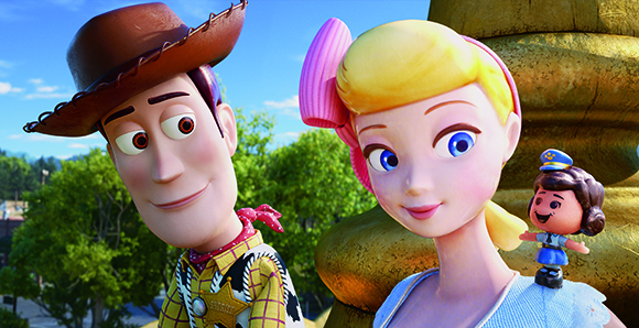 Animated Woody and Bo Peep characters smiling in front of a large golden object and green trees.