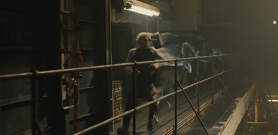 A man in dark clothing runs through a dimly lit industrial walkway holding a glowing hammer.