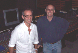 Two men wearing glasses and button-down shirts smiling in a music recording studio.
