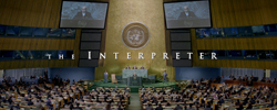 A wide shot of a large assembly hall with the title 'The Interpreter' displayed across the center.