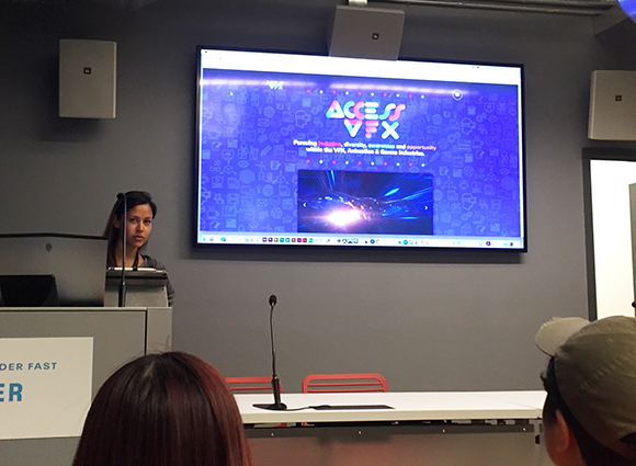 A woman stands beside a large monitor displaying a blue presentation slide for Access VFX in a dark room.
