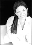 A smiling woman with long dark hair wearing a white shirt against a dark background.