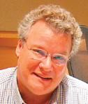 A man with curly light hair and glasses smiling slightly.