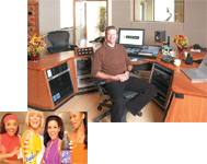 A man sits in an office chair behind a large wooden desk filled with audio mixing equipment and computer monitors.