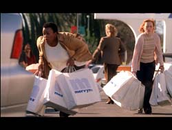 Two women walk through a parking lot carrying numerous large white shopping bags.